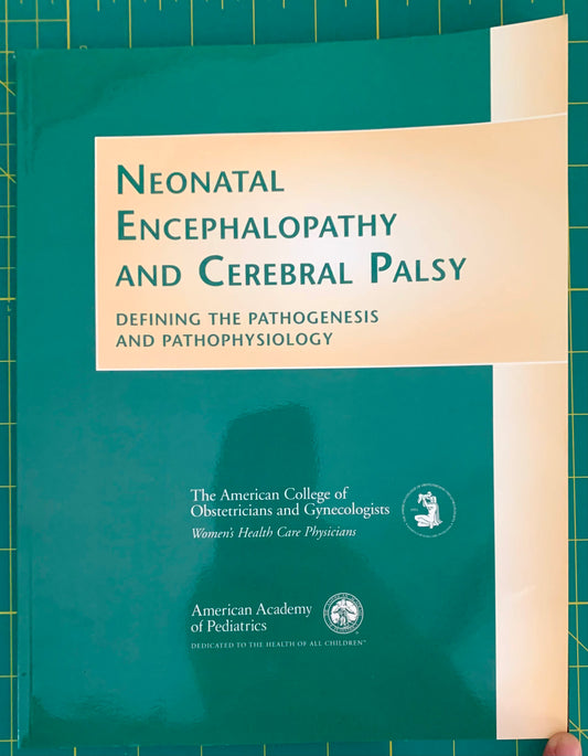 A softcover book titled 'Neonatal Encephalopathy and Cerebral Palsy' lying on a green cutting mat. The cover is green with a large cream-colored title block and white vertical bands, with publisher logos for the American Academy of Pediatrics and The American College of Obstetricians and Gynecologists visible.
[image_link]
