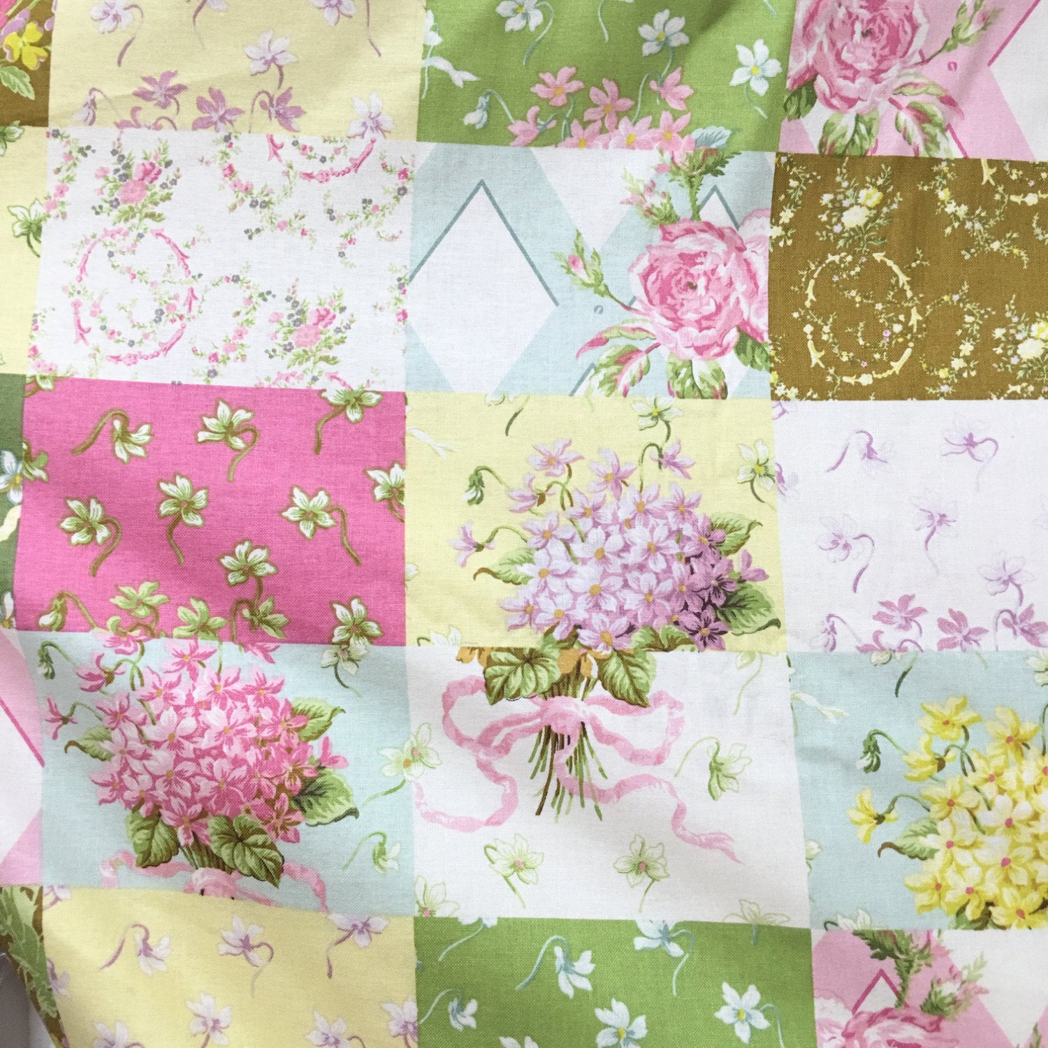 A close-up of a patchwork fabric featuring multiple square panels with floral and botanical prints in pink, green, yellow, white, and light blue, including roses, flowers, leaves, and abstract floral motifs.
[additional_image_link]