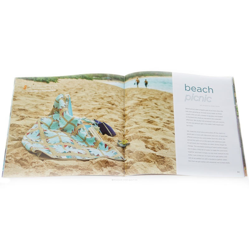 An open magazine or brochure spread on a white background, featuring a beach picnic scene with a light blue and beige patterned blanket on sand and a text column titled 'beach picnic'.
[additional_image_link]