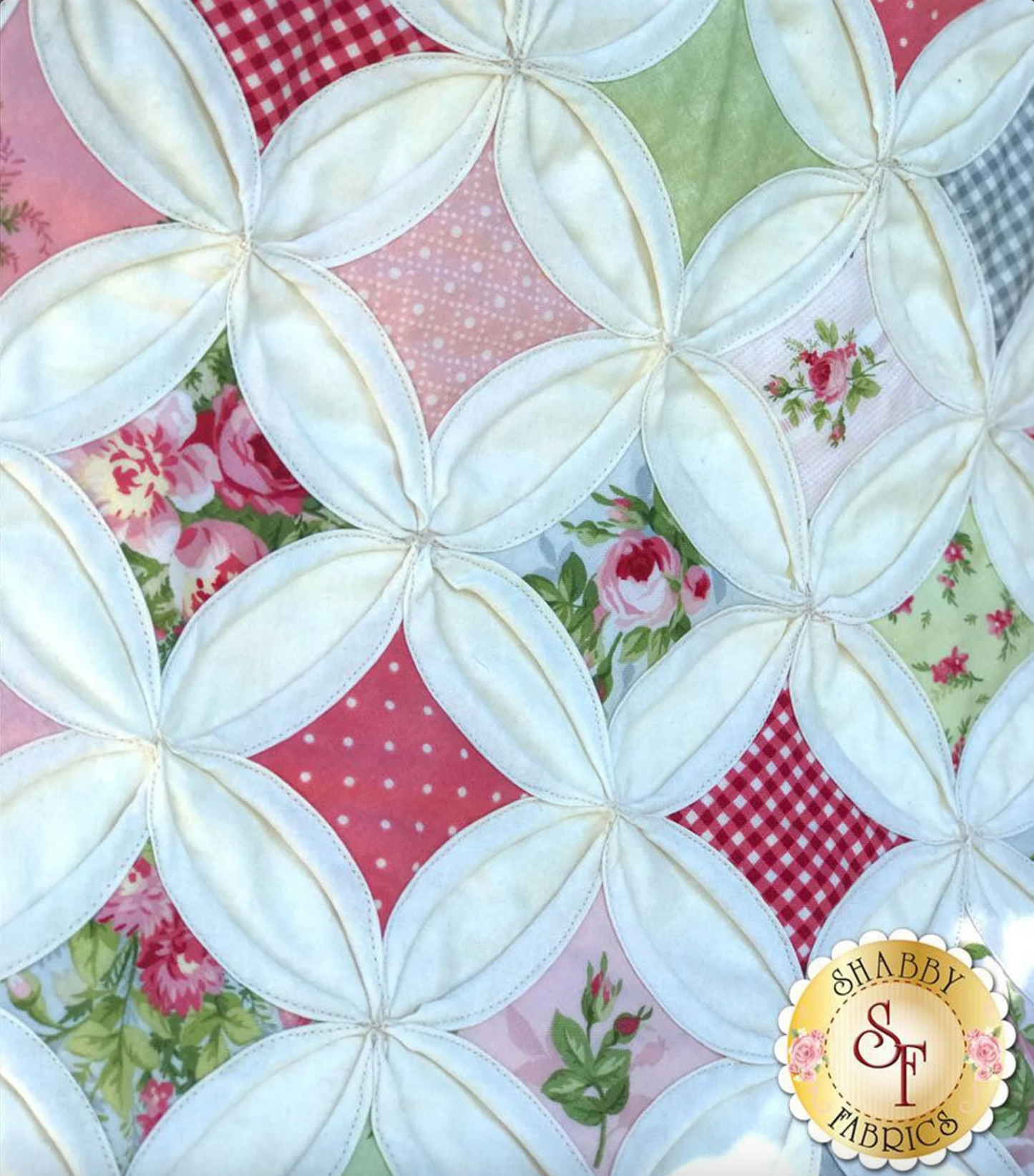 A quilt and pillow set featuring a cathedral window pattern with multicolored patches, showcased on a white chair outdoors. Close up.
Photo by Shabby Fabrics [additional_image_link]