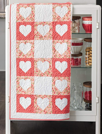 Quilt with heart patterns draped over a white cabinet.
[additional_image_link]