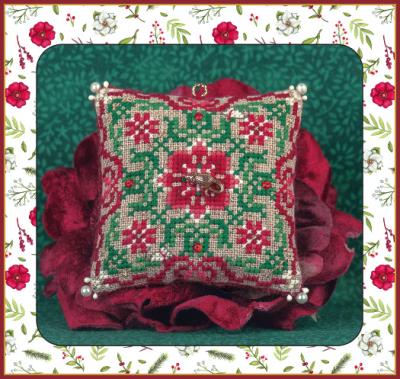 A square Christmas ornament with a embroidered design featuring a gold and red color scheme, a central gold mouse bead, and two tiny white mice with red scarves. The ornament is placed on a floral patterned fabric with green leaves and red berries, and a gold hanging ring is visible at the top.
Photo by JustNan.com [image_link]