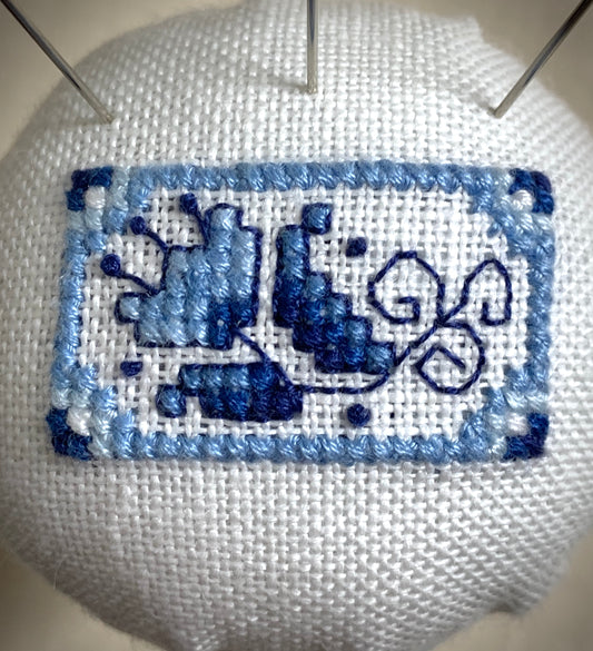 A close-up of a hand-stitched Delft pincushion with a vintage blue and white Danube double egg cup motif on white linen.
Photos by The Surgeon's Knots [image_link]