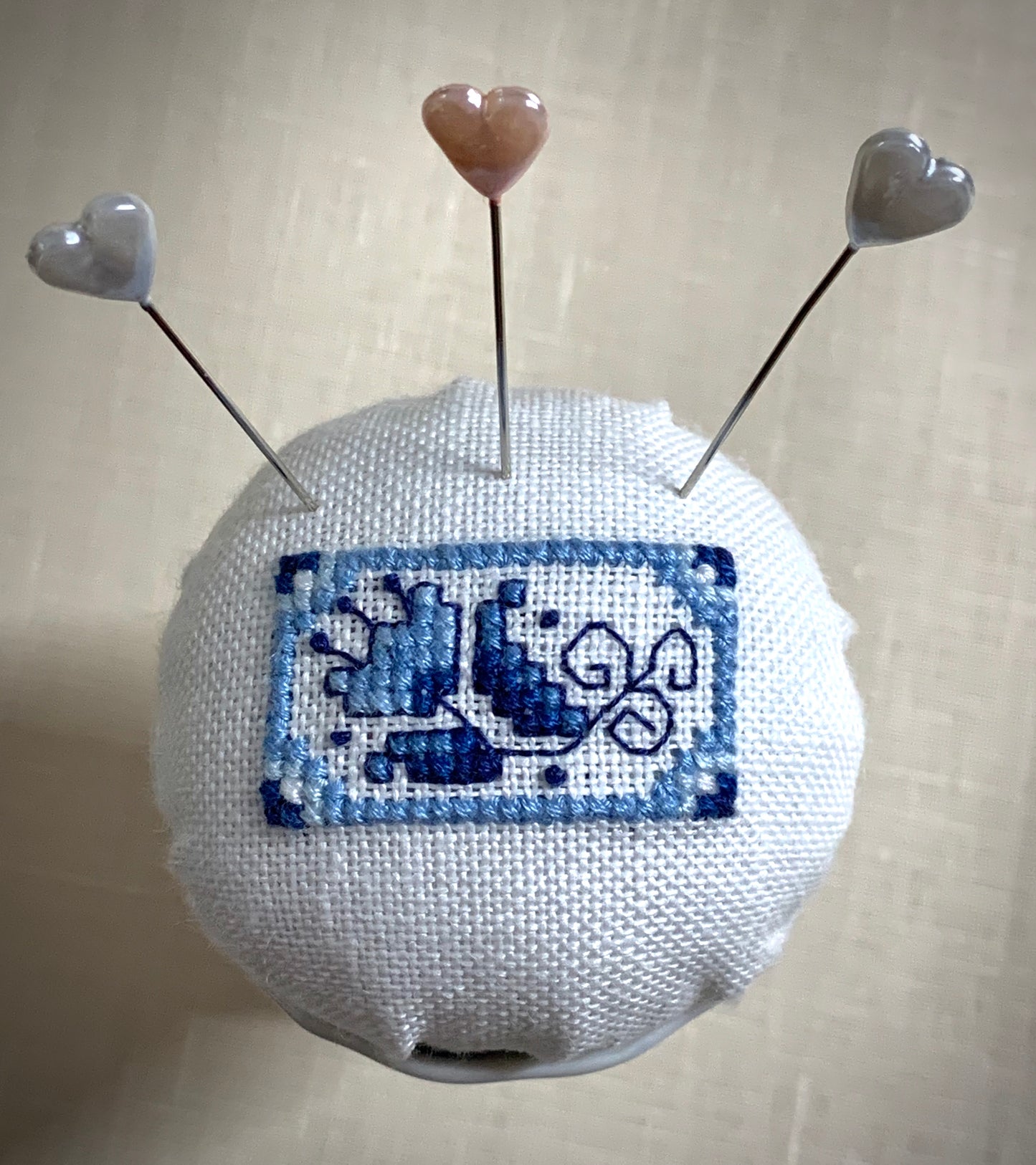A close-up of a hand-stitched Delft pincushion with a vintage blue and white Danube double egg cup motif on white linen.
Photos by The Surgeon's Knots [additional_image_link]