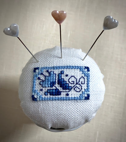 A close-up of a hand-stitched Delft pincushion with a vintage blue and white Danube double egg cup motif on white linen.
Photos by The Surgeon's Knots [additional_image_link]