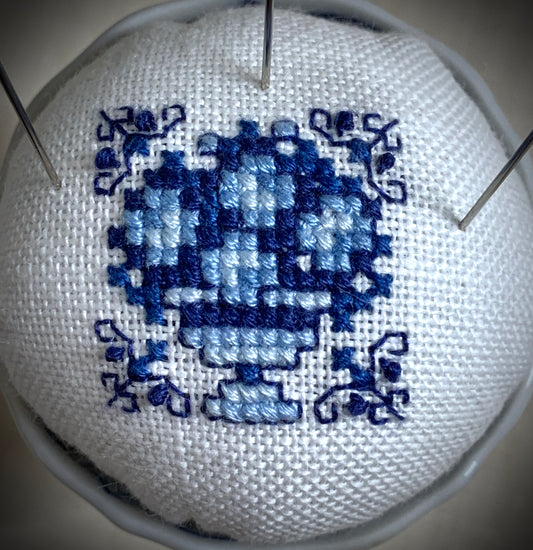 A close-up of a hand-stitched Delft pincushion with a vintage blue motif on white linen, featuring a blue and white porcelain double egg cup design.
Photos by The Surgeon's Knots [image_link]