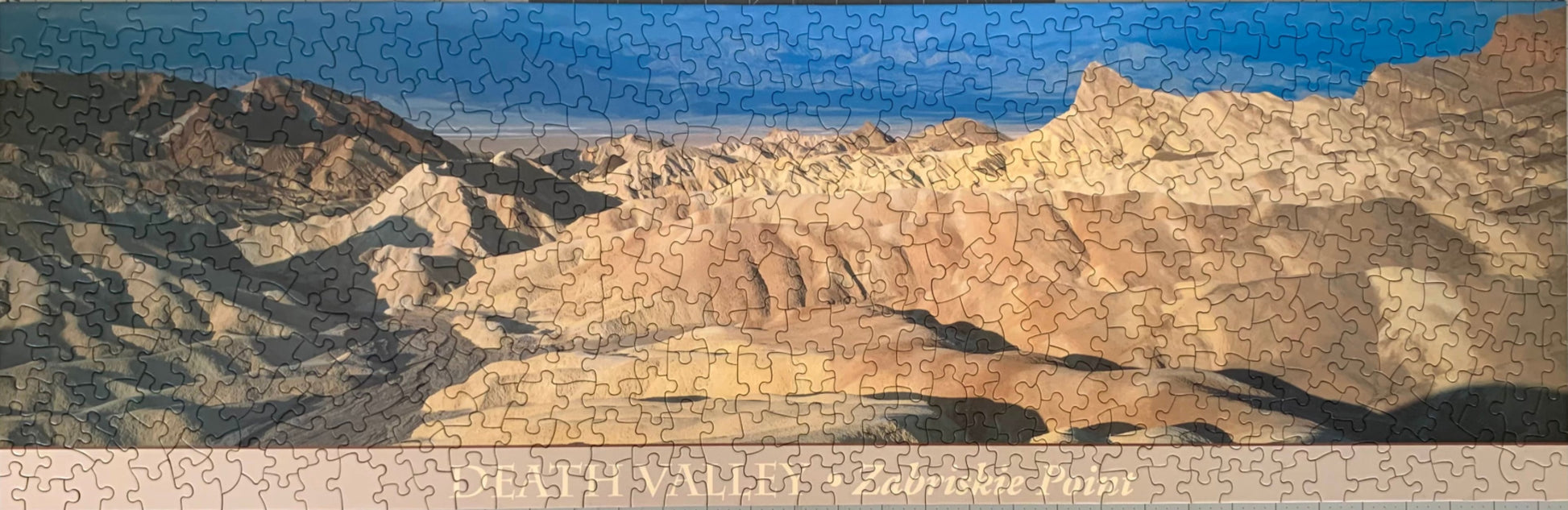 A jigsaw puzzle depicting a panoramic view of the Death Valley landscape, including the Zabriskie Point area, with a blue sky and distant mountains.
Photo by Karen King [image_link]