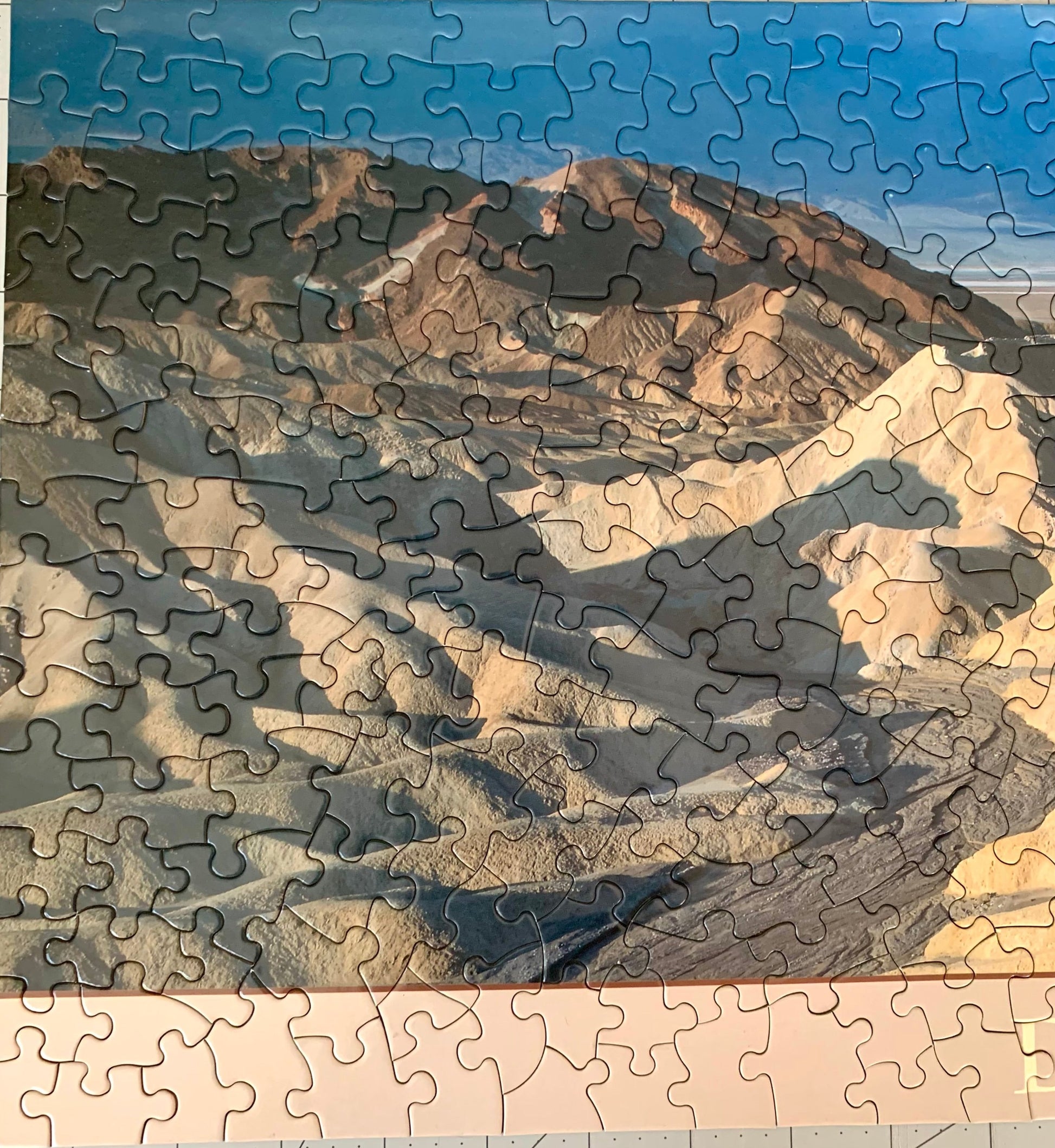 A jigsaw puzzle depicting a panoramic view of the Death Valley landscape, including the Zabriskie Point area, with a blue sky and distant mountains.
Photo by Karen King [additional_image_link]