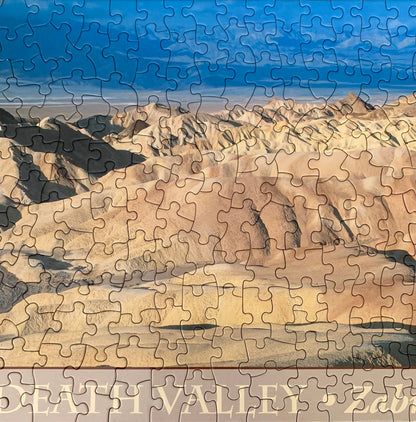 A jigsaw puzzle depicting a panoramic view of the Death Valley landscape, including the Zabriskie Point area, with a blue sky and distant mountains.
Photo by Karen King [additional_image_link]