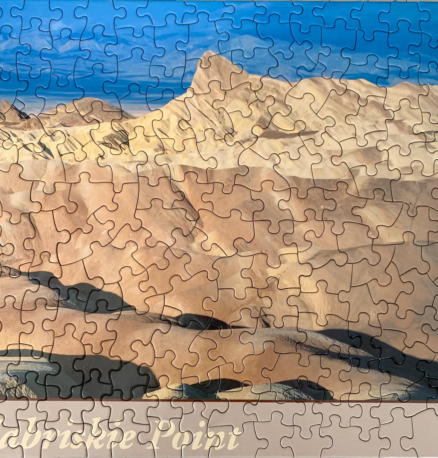A jigsaw puzzle depicting a panoramic view of the Death Valley landscape, including the Zabriskie Point area, with a blue sky and distant mountains.
Photo by Karen King [additional_image_link]