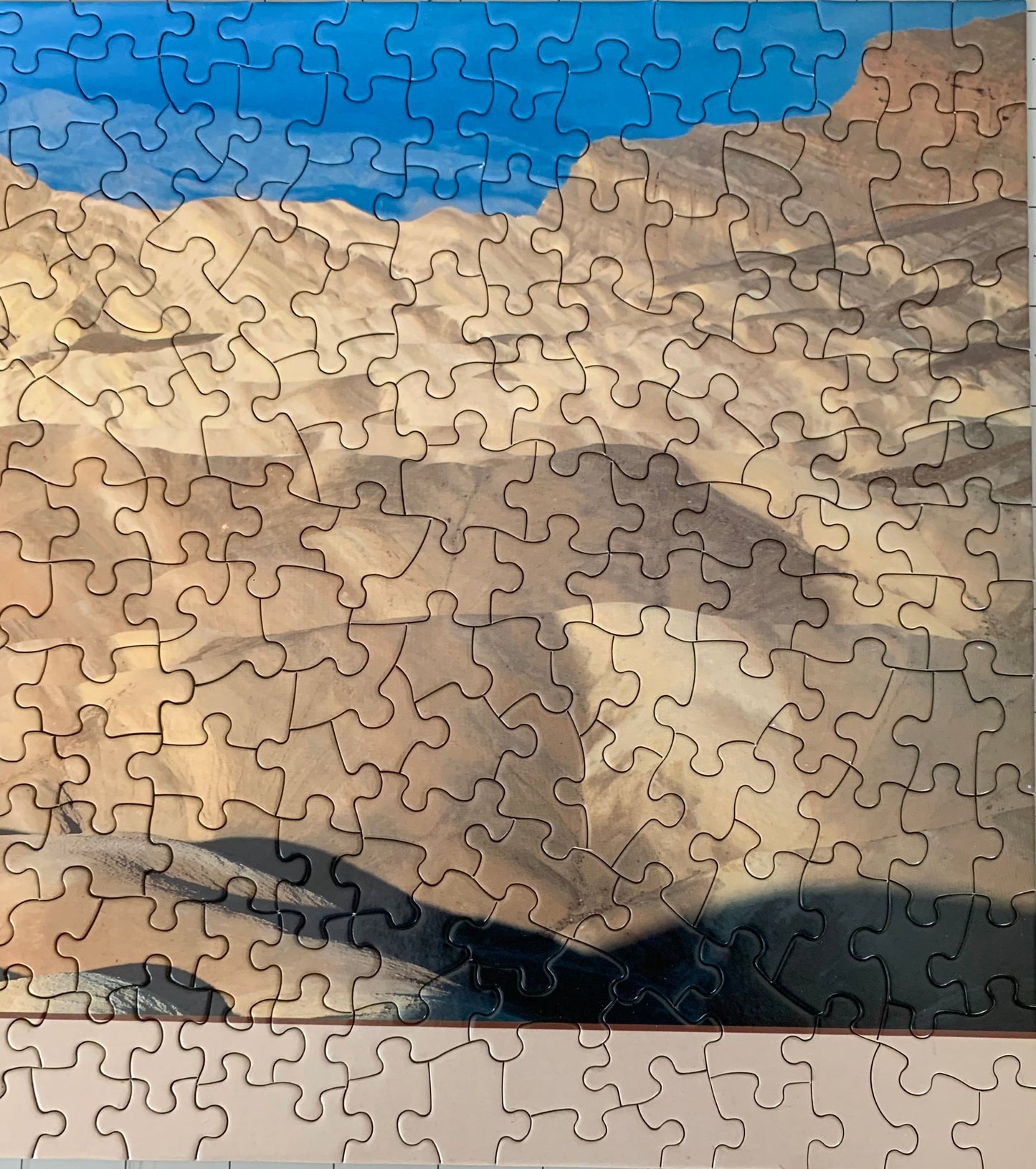 A jigsaw puzzle depicting a panoramic view of the Death Valley landscape, including the Zabriskie Point area, with a blue sky and distant mountains.
Photo by Karen King [additional_image_link]