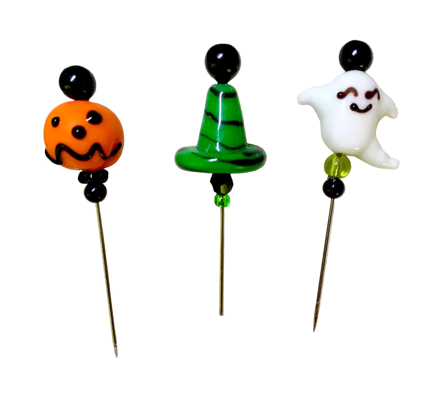 Three Halloween-themed glass pins on metal needles, featuring an orange jack-o'-lantern, a green witch hat with black stripes, and a white smiling ghost, all set against a plain white background.
[image_link]