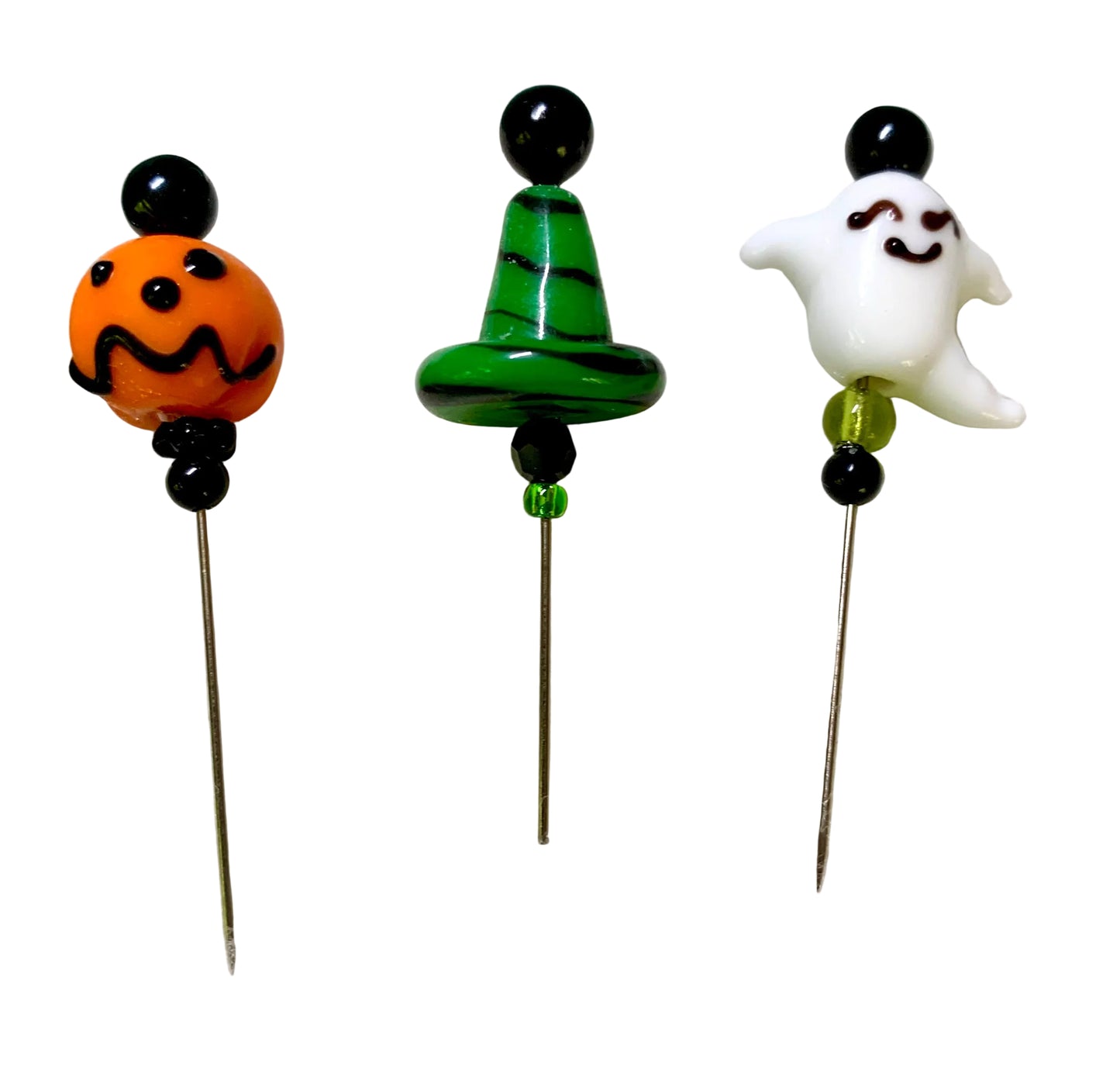 Three Halloween-themed glass pins on metal needles, featuring an orange jack-o'-lantern, a green witch hat with black stripes, and a white smiling ghost, all set against a plain white background.
[additional_image_link]