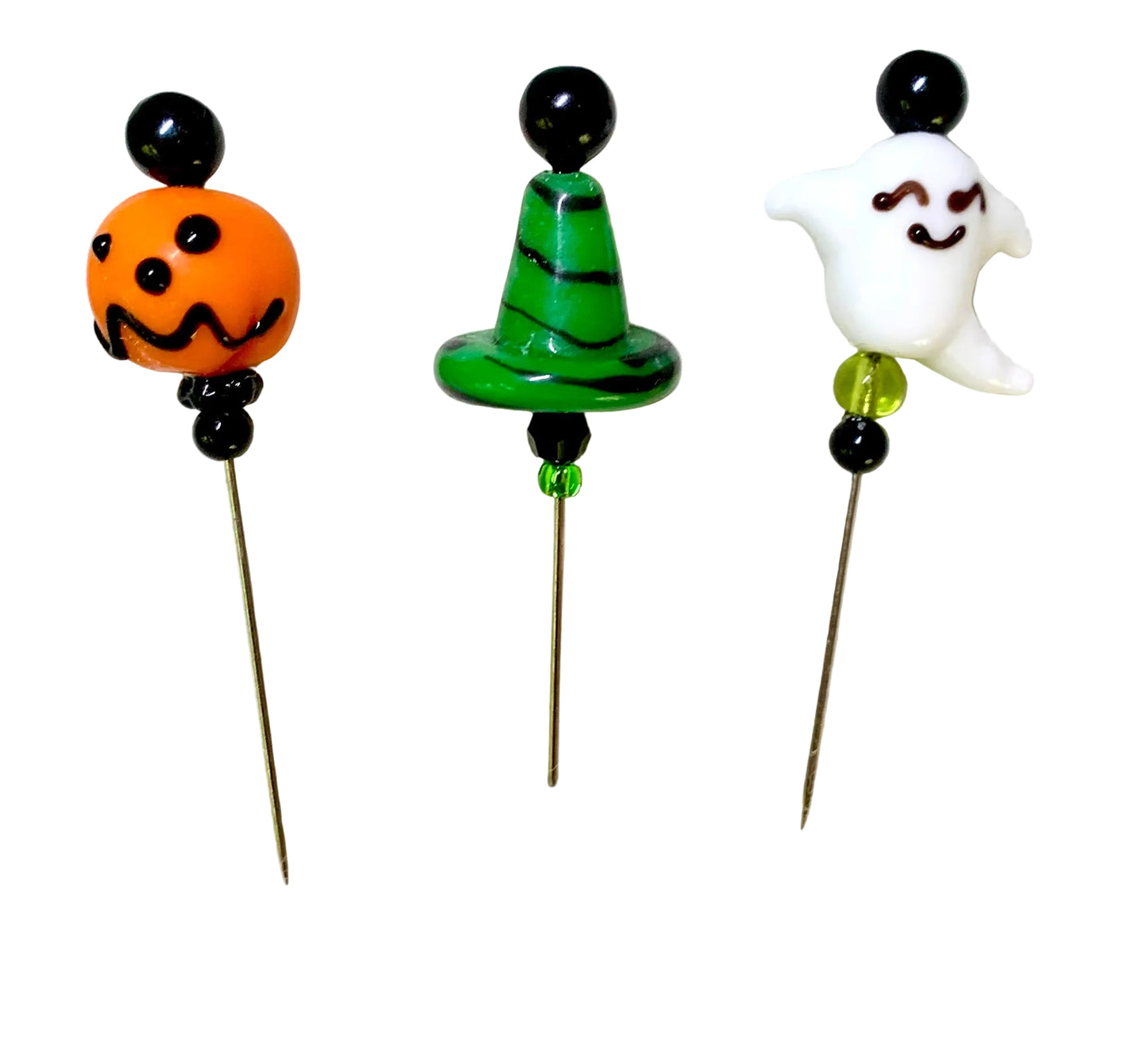 Three Halloween-themed glass pins on metal needles, featuring an orange jack-o'-lantern, a green witch hat with black stripes, and a white smiling ghost, all set against a plain white background.
[additional_image_link]