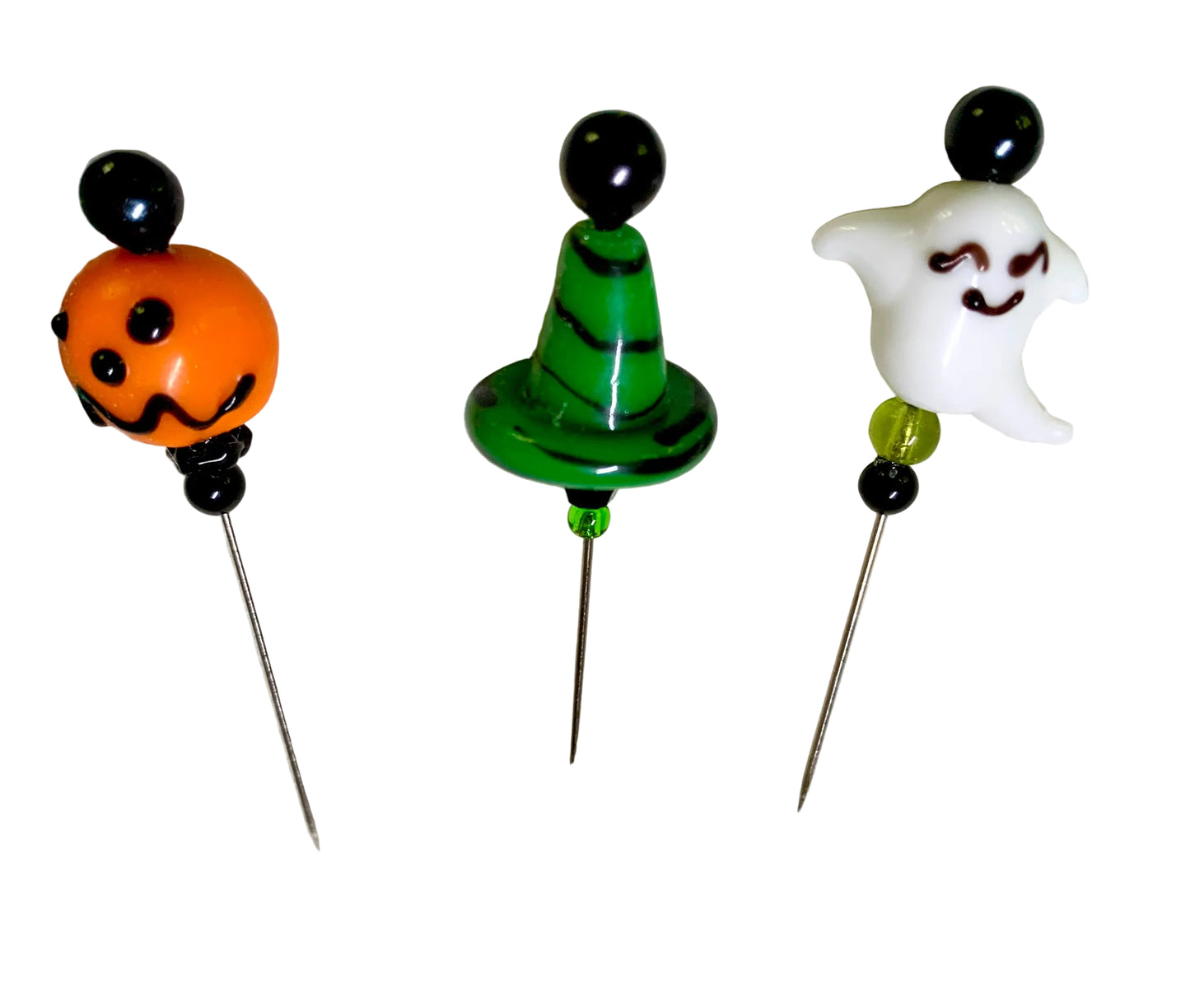 Three Halloween-themed glass pins on metal needles, featuring an orange jack-o'-lantern, a green witch hat with black stripes, and a white smiling ghost, all set against a plain white background.
[additional_image_link]