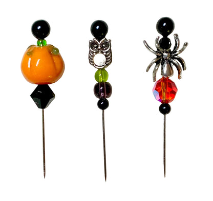 Three Halloween-themed beaded pins on a textured white background. The left pin features an orange pumpkin bead and a black faceted gem.
[additional_image_link]