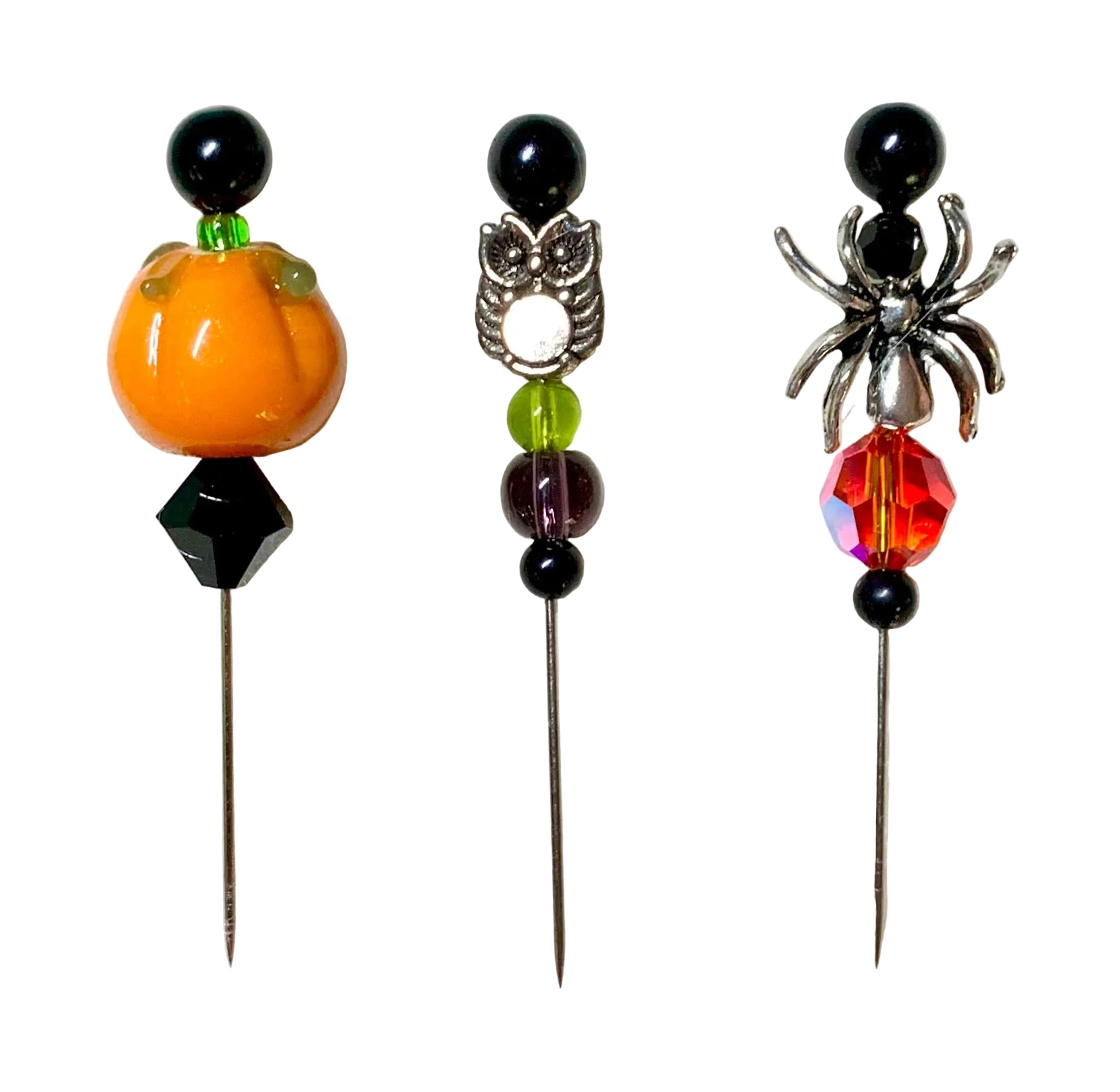 Three Halloween-themed beaded pins on a white background. The left pin features an orange pumpkin and a black diamond-shaped bead. The right pin has a silver spider with a fire bead. The middle bead has a silver owl with purple and green beads.
[additional_image_link]