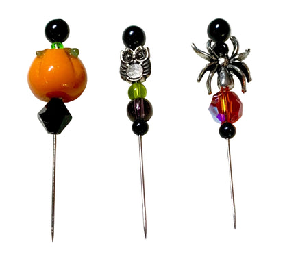 Three Halloween-themed beaded pins on metal needles, featuring an orange pumpkin, a silver owl, and a silver spider design with colorful beads, displayed on a white background.
[additional_image_link]