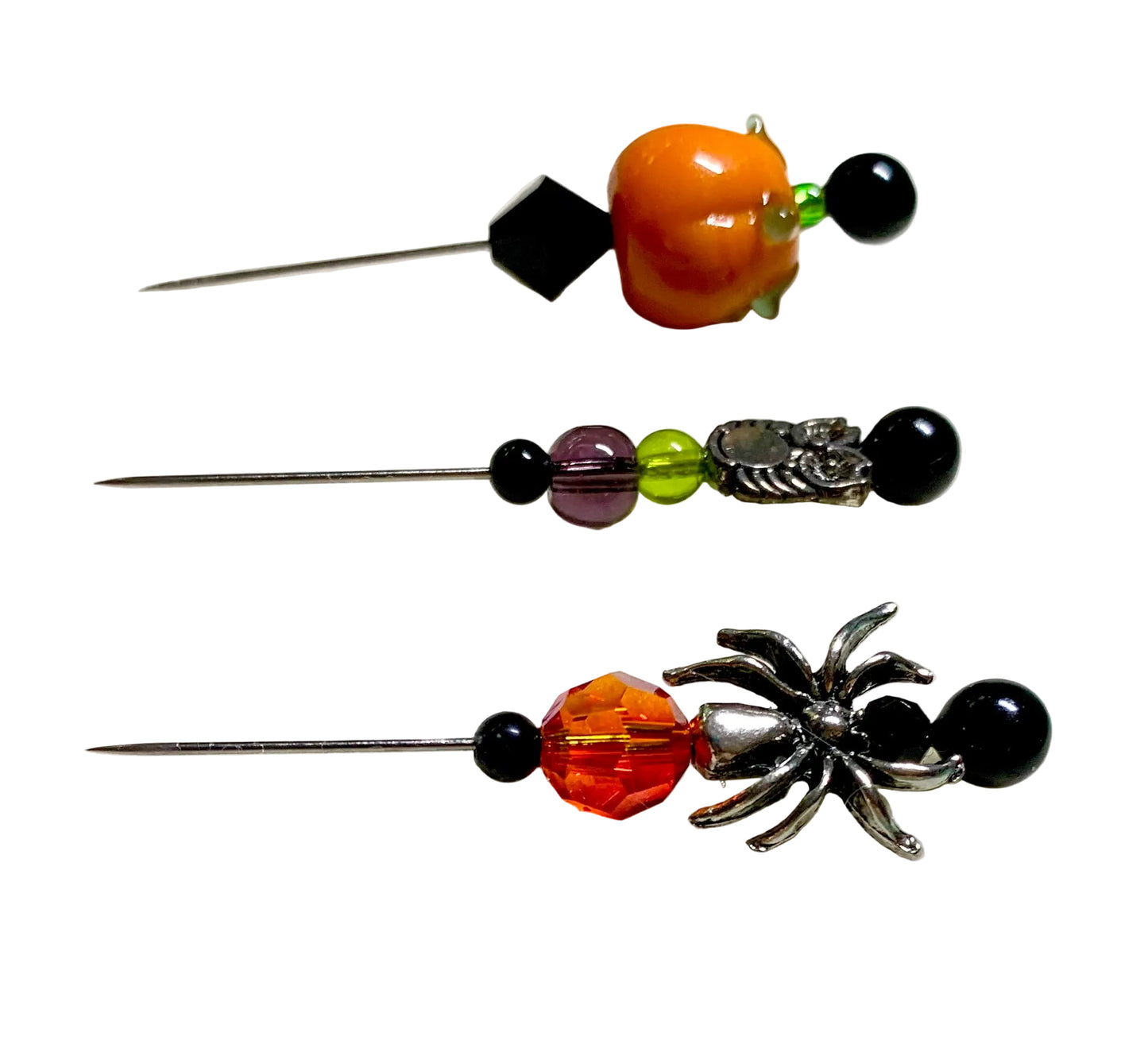 Three Halloween-themed needlepoint needles displayed on a white surface. The needles feature orange lampwork pumpkin beads, black beads, a purple bead, a green bead, a silver owl figure, and a silver spider detail.
[additional_image_link]