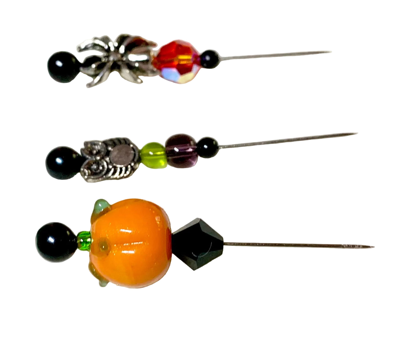 Three decorative pins with metal needles, featuring black beads, silver spider charms, a silver owl charm, a green bead, a purple bead, and an orange pumpkin bead on a white background.
[additional_image_link]