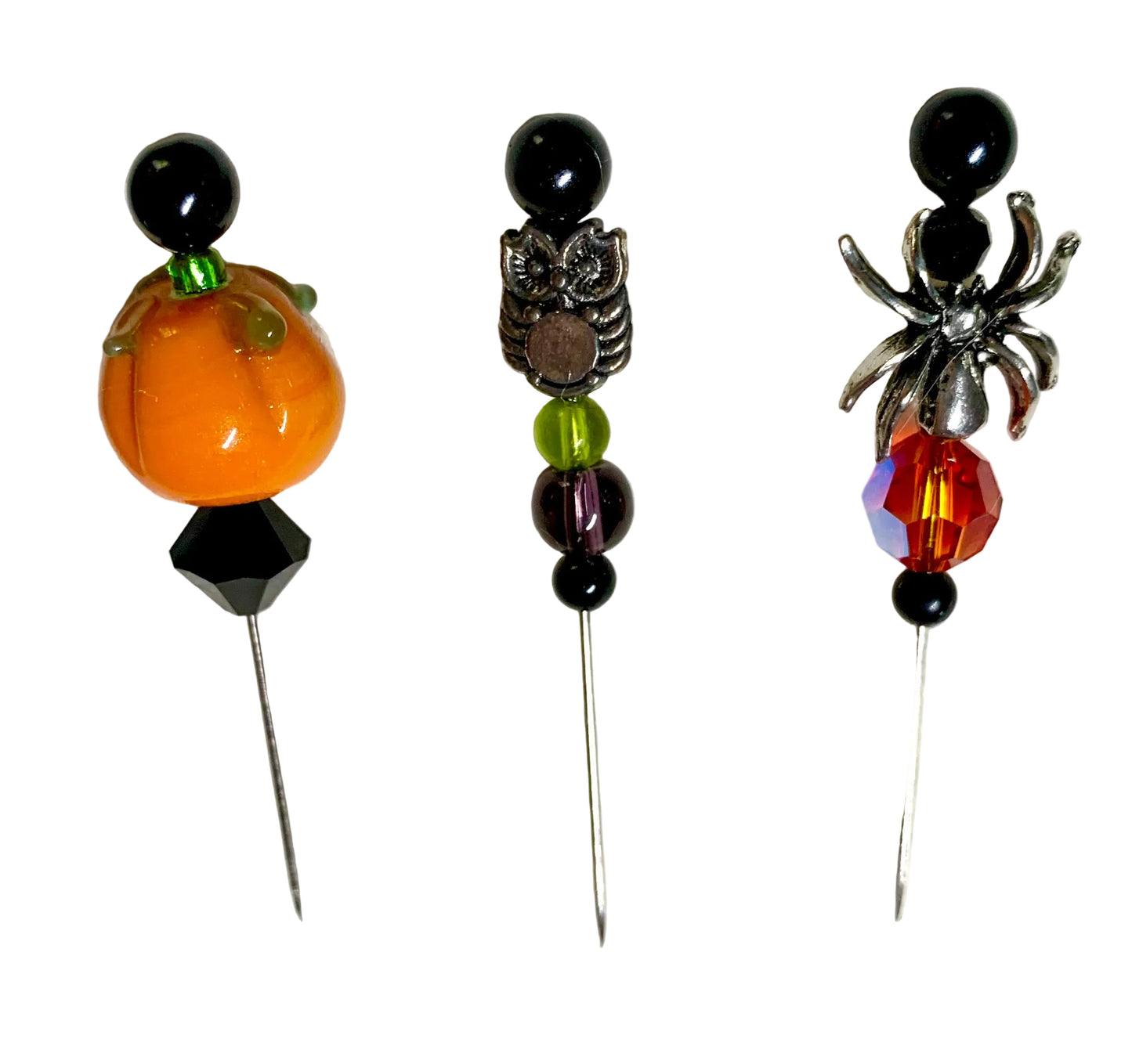 Three Halloween-themed beaded pins on a white background. The left pin features an orange pumpkin bead with a green stem and black beads. The middle has a silver owl charm and the right pin has a silver spider charm.
[additional_image_link]
