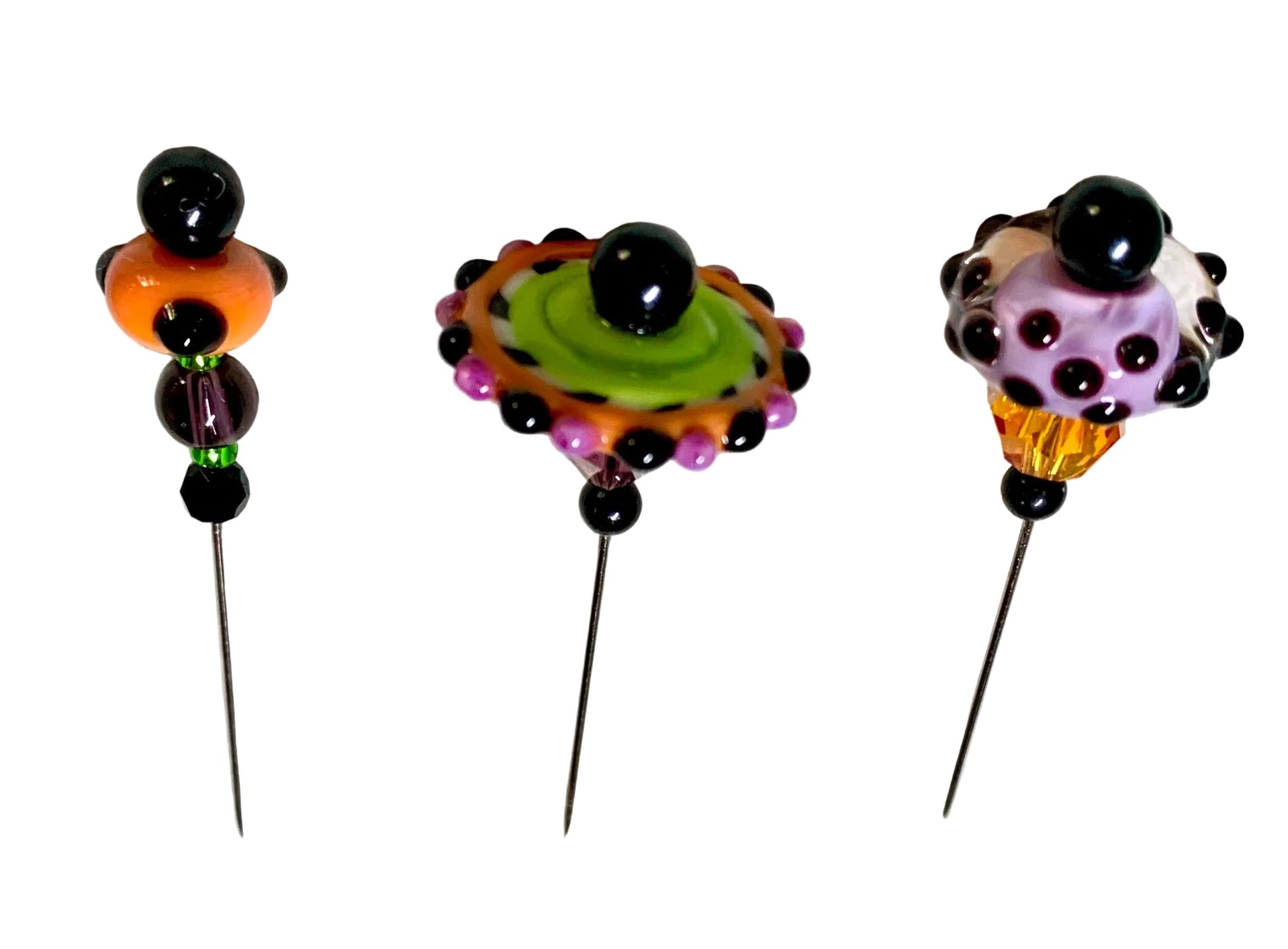 Three handmade lampwork bead pins with long black metal needles, displayed on a white background. The beads feature colorful glass designs including purple, green, orange, and black.
[additional_image_link]