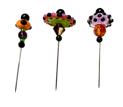 Three decorative beaded pins with long metal needles, displayed on a white surface. The left pin has orange, black, and green beads; the middle pin features a multicolor beaded fan design with green, orange, purple, and black beads; the right pin has a lavender and black beaded top with an orange faceted bead.
[additional_image_link]