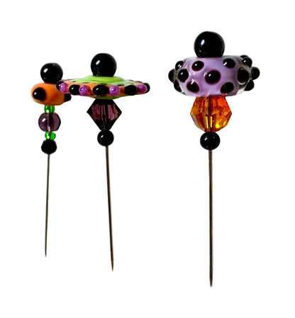Three handmade beaded pins with long metal needles, featuring colorful glass beads including black, purple, orange, green, and white polka dots, displayed on a white surface.
[additional_image_link]