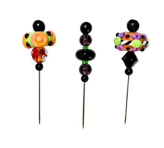 Three decorative glass bead pins, displayed on a white surface. The pins feature orange, green, and black beads with a faceted orange and red accent.
[image_link]