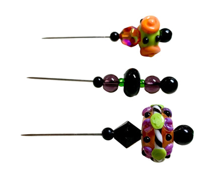 Three handmade beaded pins with long metal needles, displayed on a white surface. The pins feature colorful glass beads, including black, purple, orange, green, and fire.
[additional_image_link]