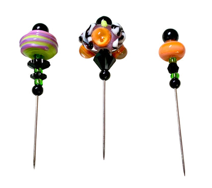 Three handmade glass pins with colorful beads and decorative tops, displayed on a white surface.
[additional_image_link]