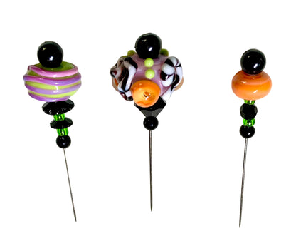 Three handmade bead pins with long metal needles, displayed on a white background. The left pin features a purple and green striped bead, the middle pin has a black, white, and orange patterned bead cluster, and the right pin has an orange bead.
[image_link]
