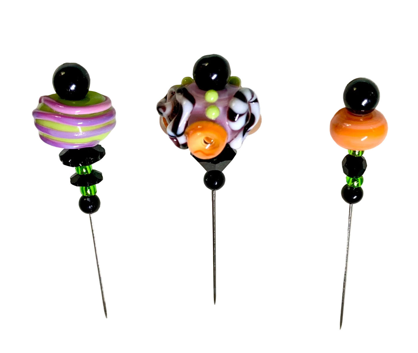 Three handmade glass bead pins with metal needles, displayed on a white background. The left pin features purple and lime green striped beads, the middle pin has a multicolor swirl of purple, black, white, and orange, and the right pin has a large orange bead.
[additional_image_link]
