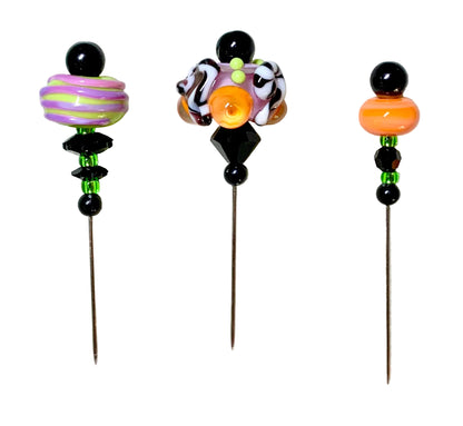 Three handmade lampwork bead pins with metal needles, displayed on a white background. Each pin features a unique colorful lampwork bead design with black beads and neon green spacer beads.
[additional_image_link]