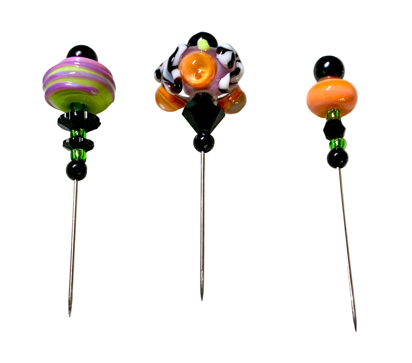 Three handmade glass bead pins with long metal needles, displayed on a white surface. The left pin features a green and purple striped bead with black accents.
[additional_image_link]