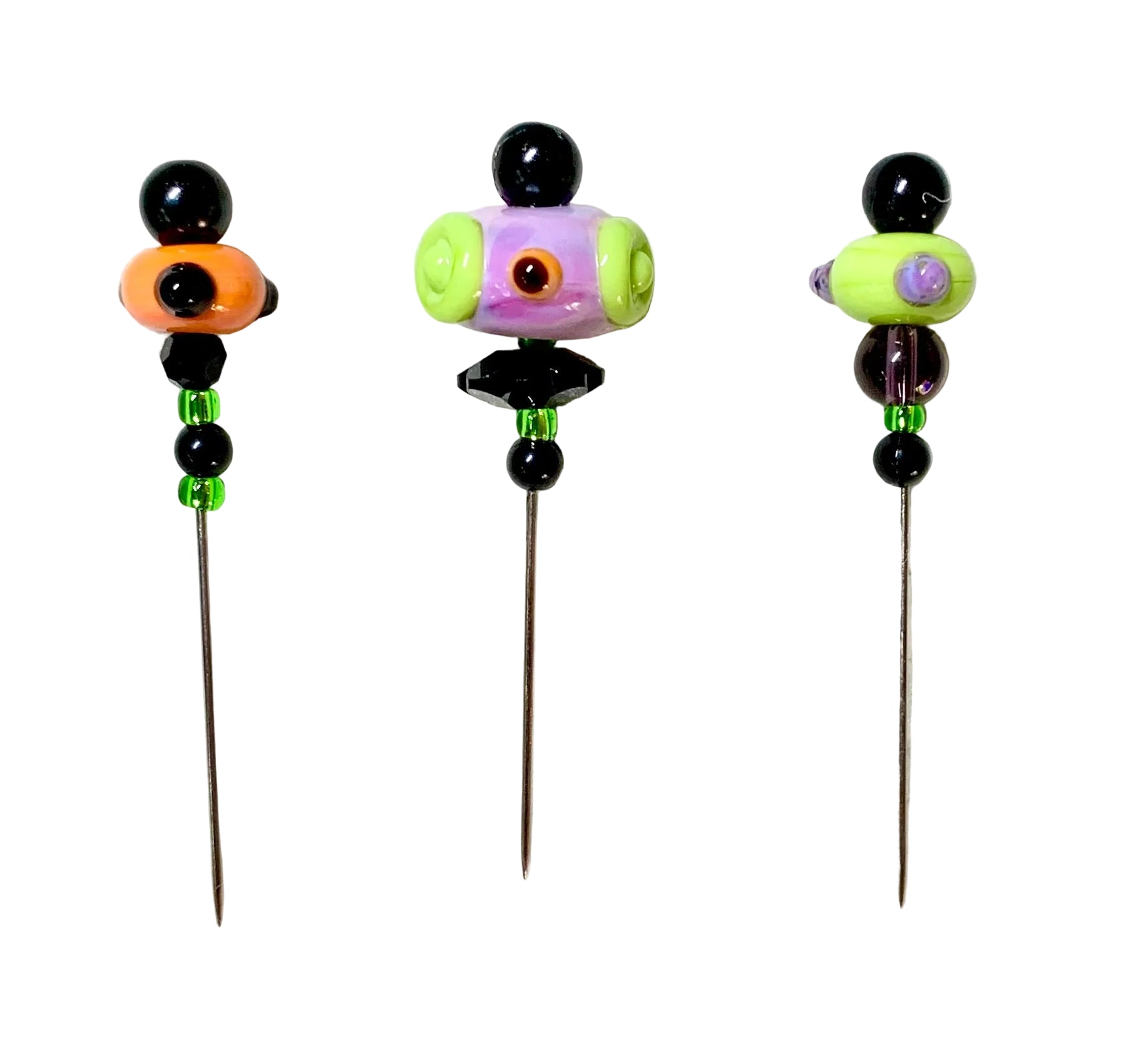 Three handmade beaded pins with long metal needles, decorated with colorful glass beads including black, orange, purple, green, and white, displayed on a white background.
[additional_image_link]