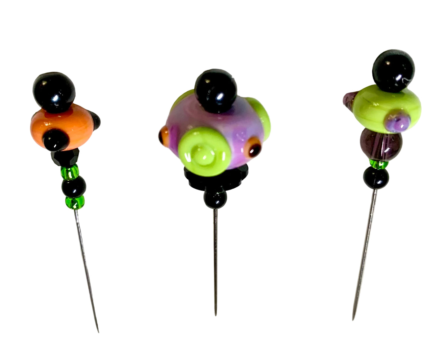 Three handmade lampwork bead pins with metal spikes, featuring colorful glass beads in orange, purple, lime green, and black, displayed on a white textured background.
[additional_image_link]