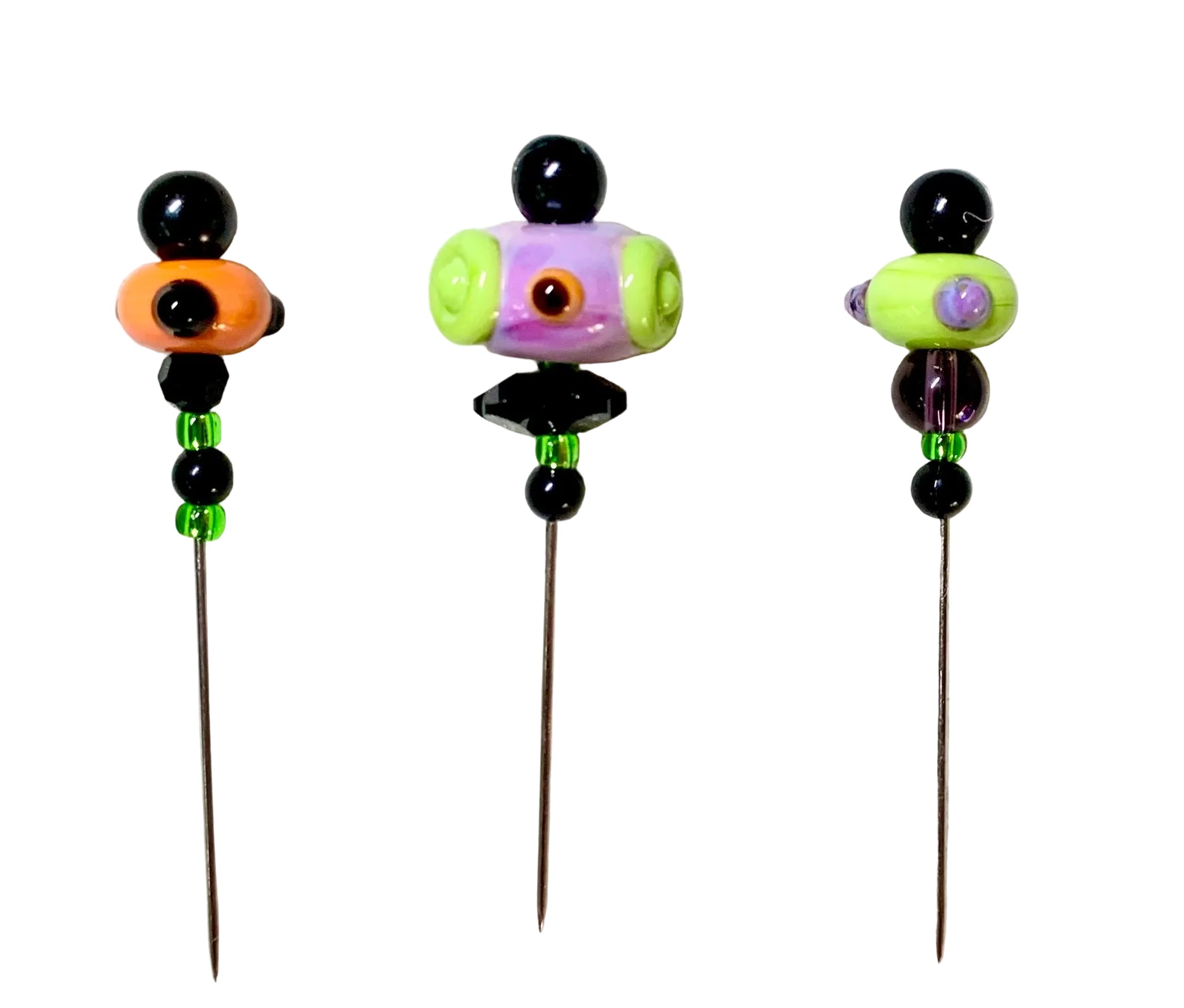 Three handmade glass bead pins with long metal needles, displayed on a textured white felt background. The beads feature black, orange, purple, green, and purple details.
[additional_image_link]