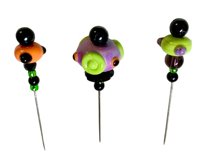 Three handmade beaded pins with colorful glass beads and metal needles, displayed on a textured white background.
[additional_image_link]