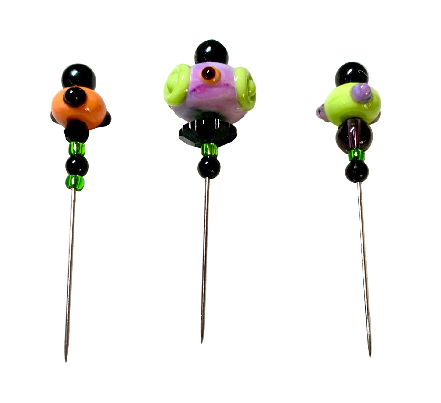 Three handmade glass bead pins with long metal needles, displayed on a white felt surface. The pins feature colorful glass beads including black, orange, green, purple, and yellow.
[additional_image_link]