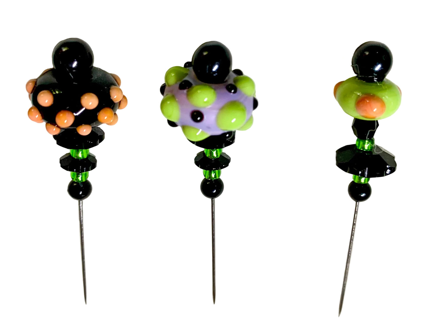 Three handmade glass pinback beads with long metal pins, displayed on a white background. Each bead features a unique colorful pattern of black, lime green, purple, and orange.
[additional_image_link]