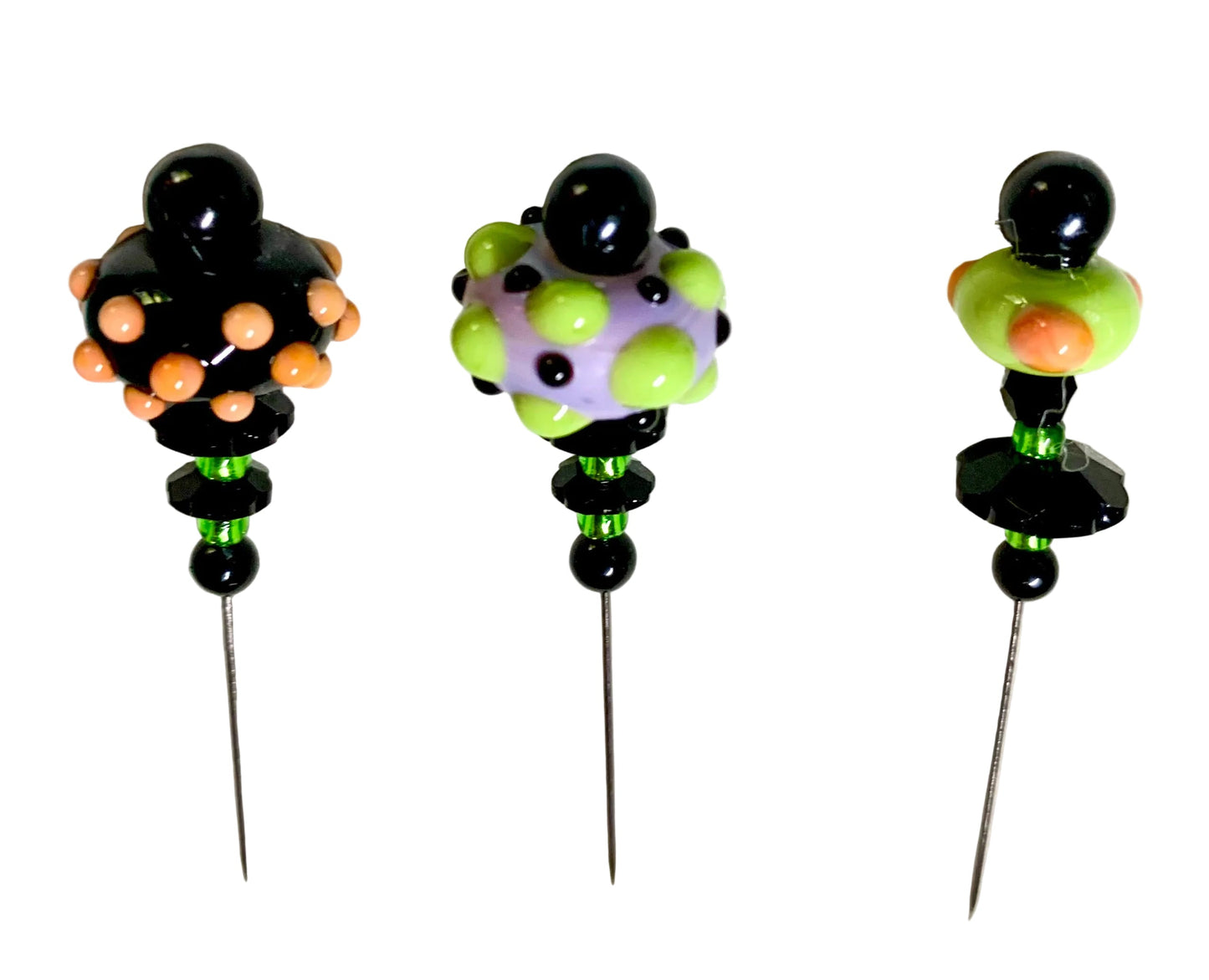 Three decorative glass pinback pins with black metal needles, featuring colorful beaded tops in black, orange, green, and lavender on a white textured background.
[additional_image_link]