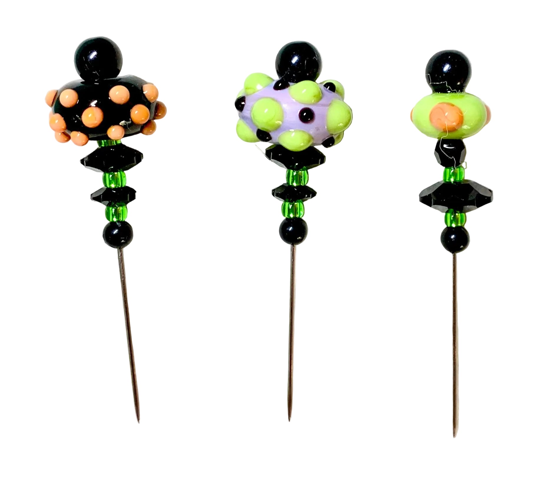 Three decorative beaded pins with long metal needles, displayed on a textured white background. Each pin features a unique colorful top section with black beads and green faceted beads.
[additional_image_link]