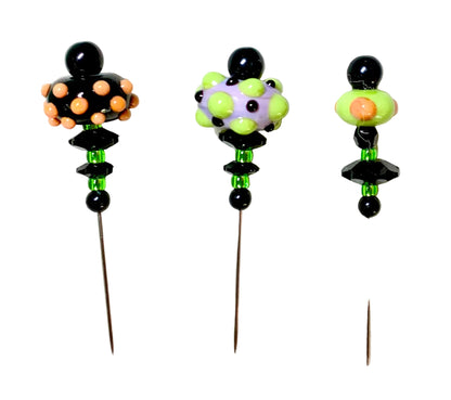Three Halloween-themed glass lampwork beads with long metal pins, displayed on a white background. The designs feature black, orange, green, and purple elements.
[additional_image_link]