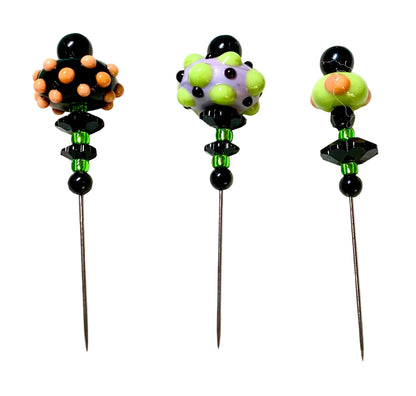 Three decorative glass beaded pins with long metal needles, displayed on a white surface. The pins feature colorful glass bead tops in black, orange, green, and purple, with green and black beads below.
[additional_image_link]