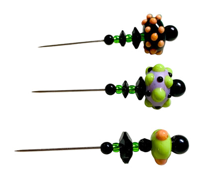 Three handmade beaded sewing pins with black and green beads and colorful decorative ends, displayed on a white surface.
[additional_image_link]