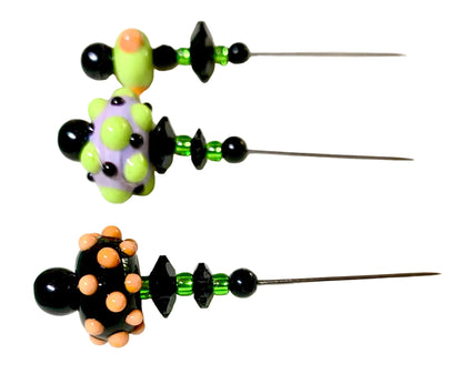 Three handmade beaded pins with long metal needles, featuring black beads, green faceted beads, and colorful glass lampwork beads in lime green, lavender, and peach, displayed on a white surface.
[additional_image_link]
