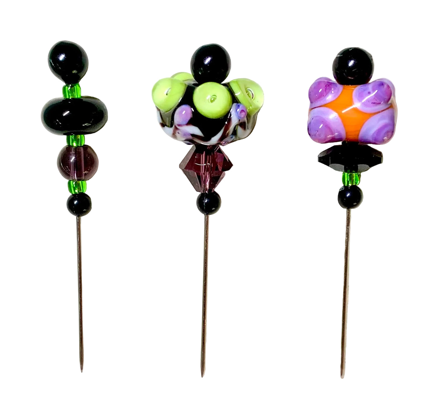 Three handmade beaded pins with long metal spikes are displayed on a white background. Each pin features a unique colorful bead design: a black and lime green design on the left, a black, purple, and lime green design in the middle, and a purple, orange, and black design on the right.
[additional_image_link]
