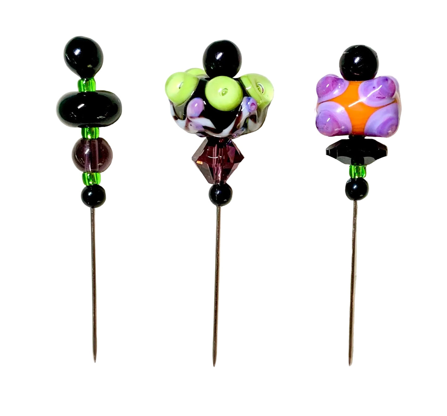 Three handmade glass bead pins with long metal spikes, displayed on a white background. The pins feature various colorful and patterned glass beads including black, purple, green, orange, and white.
[additional_image_link]