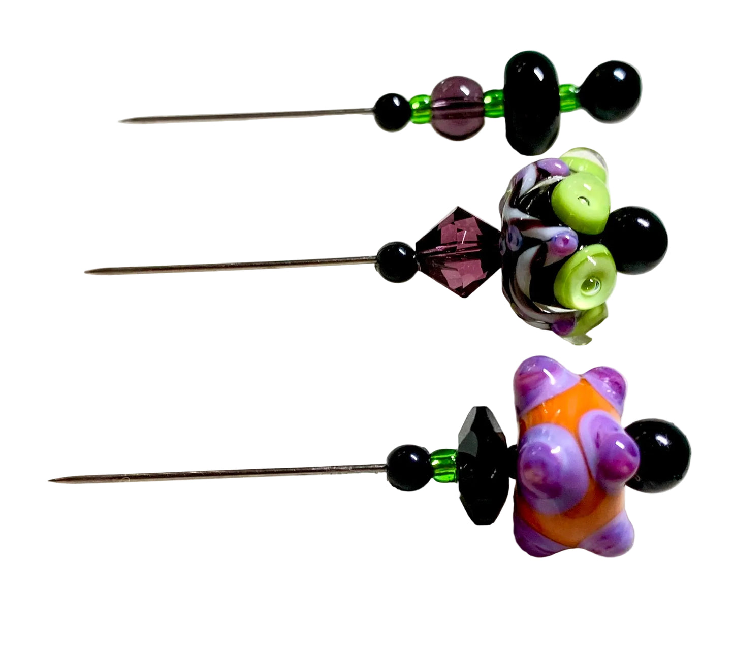 Three beaded lampwork glass beads with metal pins, featuring black beads, green beads, purple crystal accents, and colorful spider-shaped lampwork beads in purple, orange, and green, displayed on a white surface.
[additional_image_link]